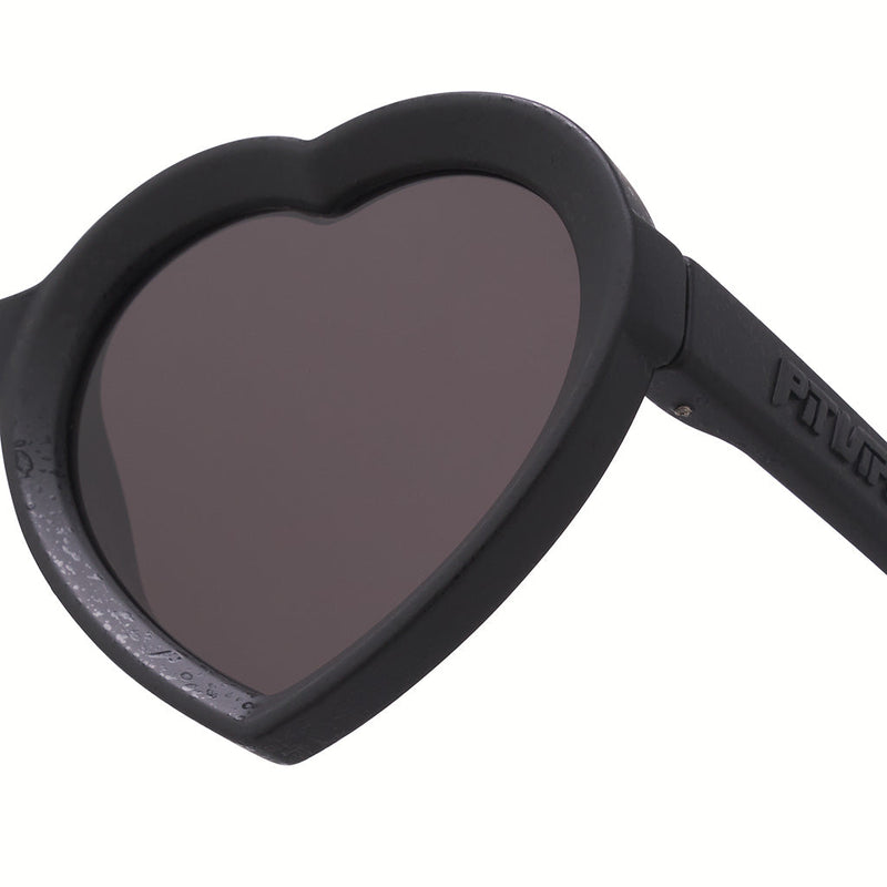 Smoke | im_ready_for_my_closeup.JPG | Close-up of heart-shaped sunglasses with a matte black frame and dark tinted lenses, showing part of the temple arm on a white background.