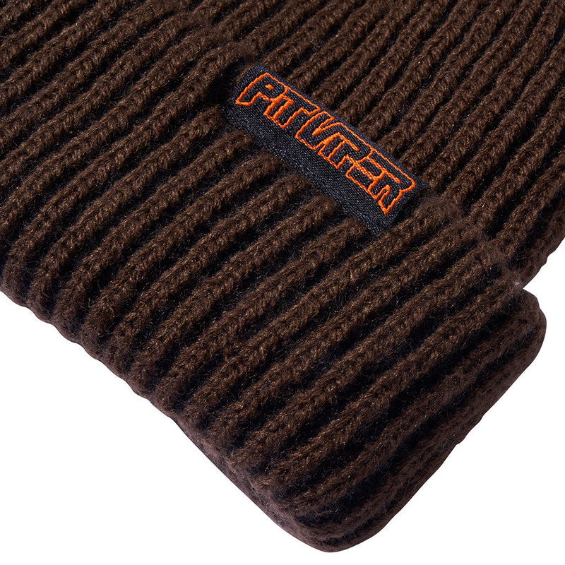 | im_ready_for_my_closeup.JPG | Close-up of a dark brown ribbed knit beanie with a folded cuff and an embroidered black patch 
