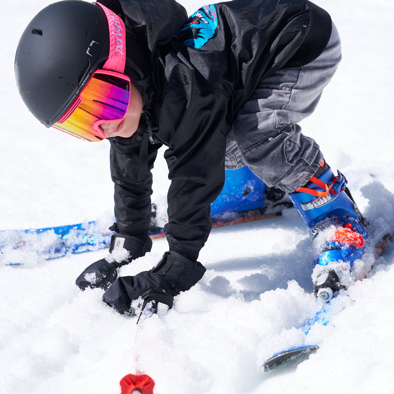 | photo_of_skier.JPG | A child in a black ski jacket, black helmet, and colorful mirrored goggles bends down in deep snow, adjusting a blue snowboard or ski base near their boots.