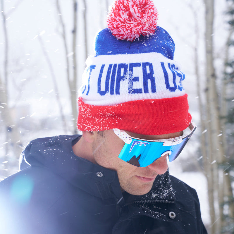 | photo_of_nick_g.JPG | A man wearing a red, white, and blue knit beanie with a pom-pom and the words 'NOT VIPER USA' on the front, along with blue mirrored ski goggles and a dark winter jacket, standing in the snow with trees blurred in the background.