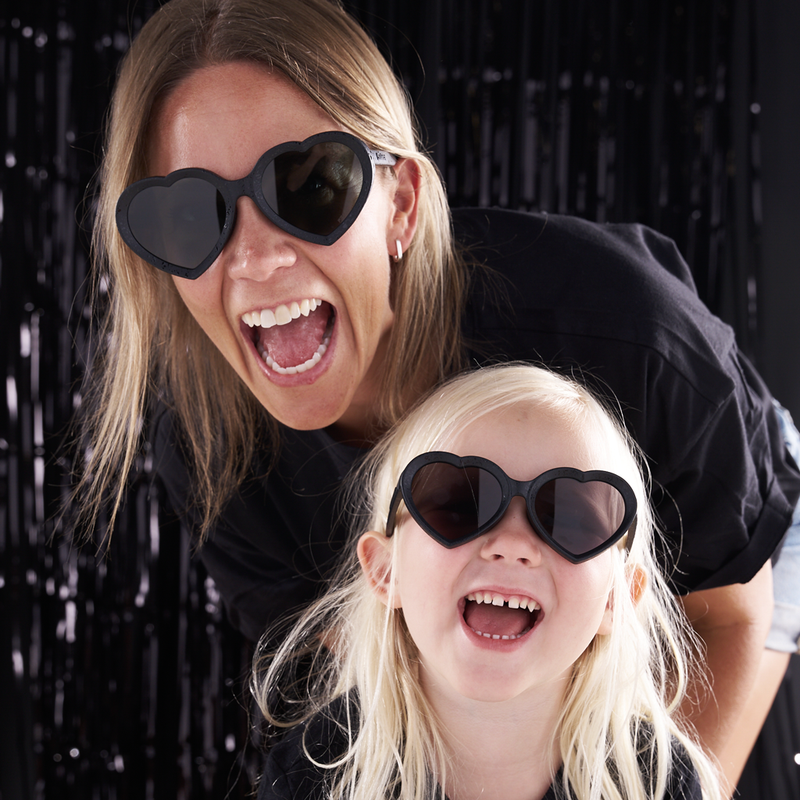 Smoke | you_can_match_mom.JPG | A woman and a young girl wearing black heart-shaped sunglasses with dark lenses, smiling and laughing in front of a black tinsel curtain background