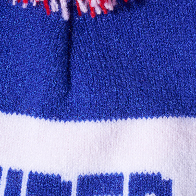 | im_ready_for_my_closeup.JPG | Close-up of a knitted textile product, likely a beanie or hat, showing a royal blue knit body, a wide white band, and a small red and white tassel at the top.